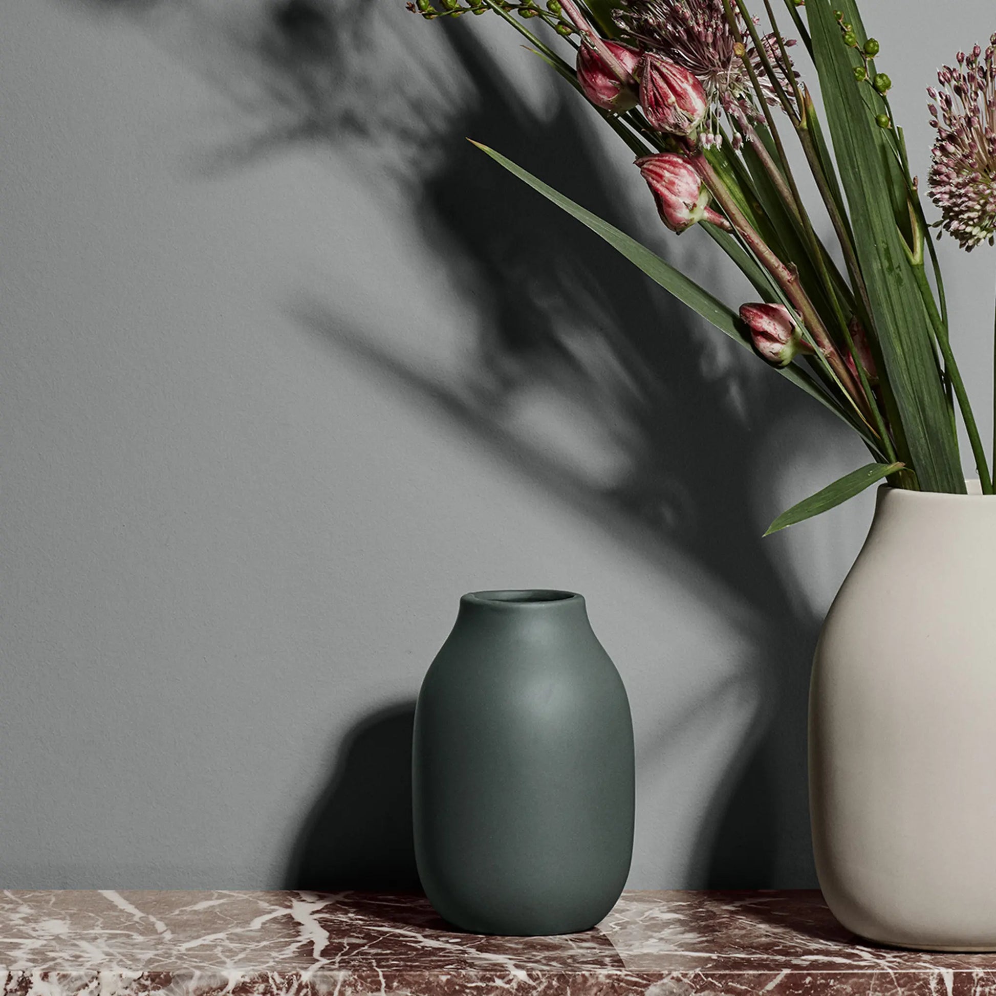 Colora porslinsvas i grön färg med en större vit vas med blomster i