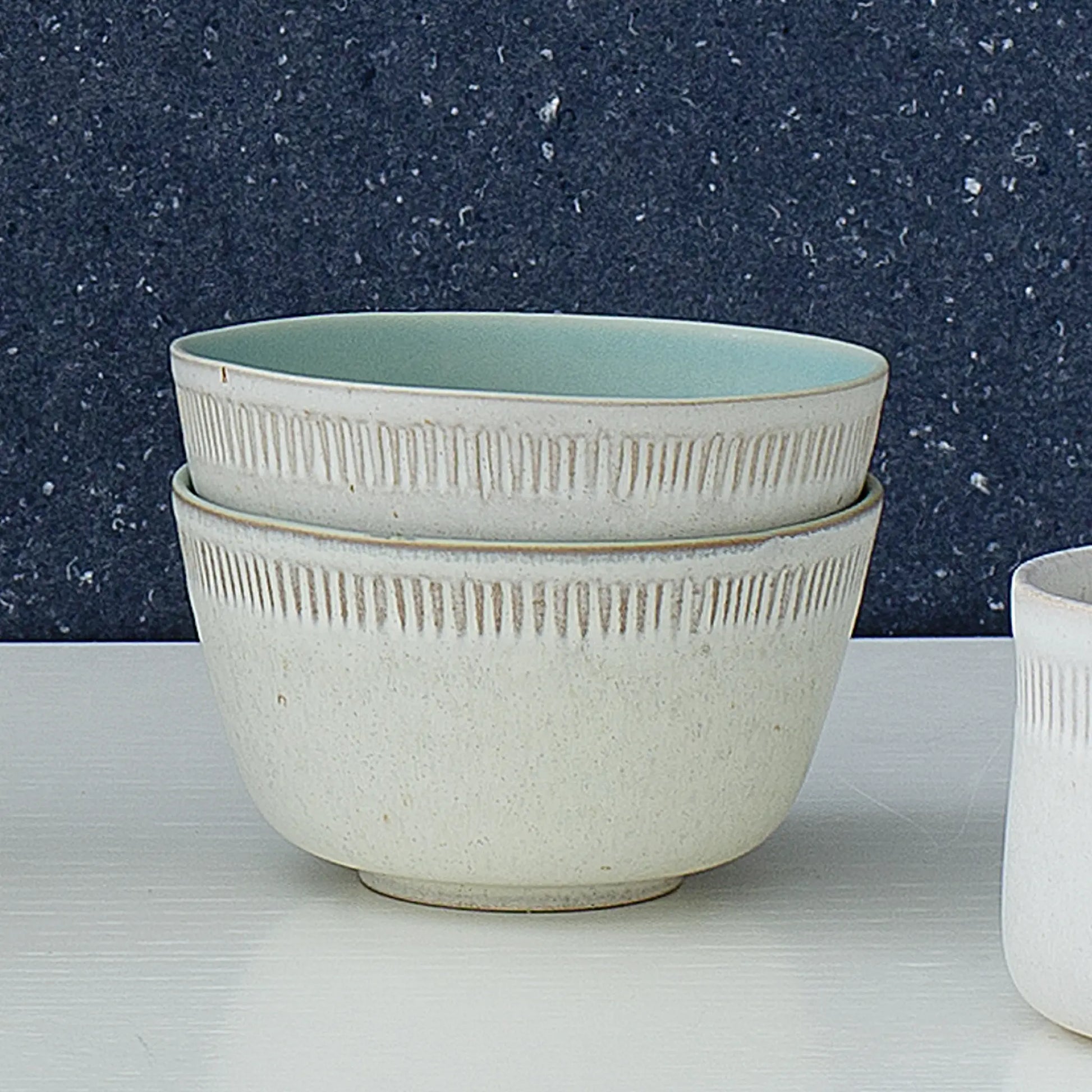 Två stycken The Food Bowl skålar från Spring Copenhagen i keramik mot en blå bakgrund